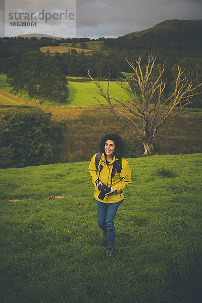 Hochwinkelaufnahme einer glücklichen Frau mit Kamera auf einem grasbewachsenen Hügel