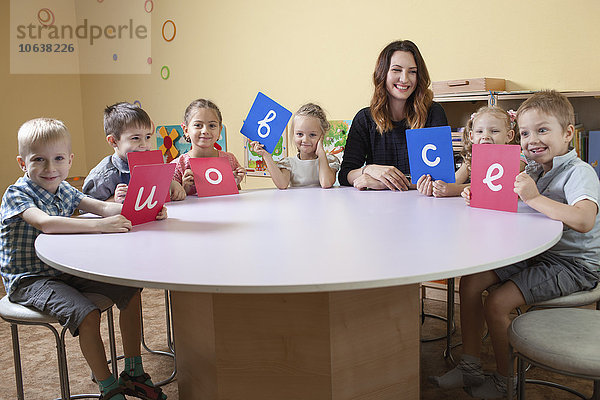 Porträt eines glücklichen Lehrers mit Kindern mit Alphabetkarten am Tisch im Klassenzimmer