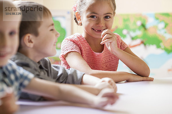 Porträt eines glücklichen kleinen Mädchens mit Freunden am Tisch im Klassenzimmer