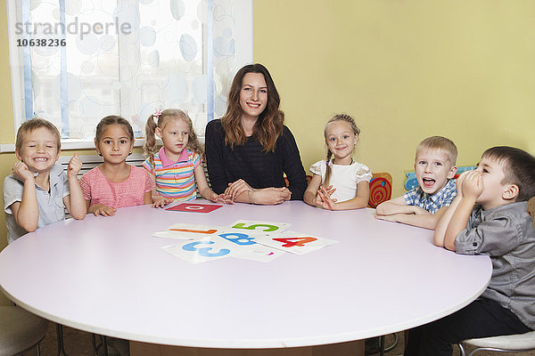 Porträt eines glücklichen Lehrers mit Kindern am Tisch im Klassenzimmer