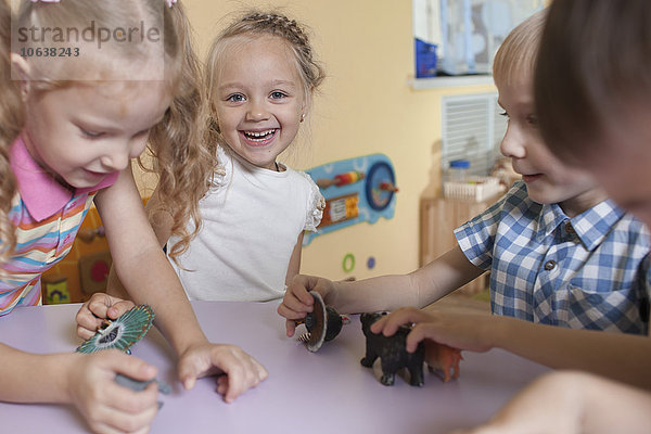 Porträt eines fröhlichen Mädchens mit Freunden  die mit Spielzeugtieren bei Tisch im Klassenzimmer spielen.