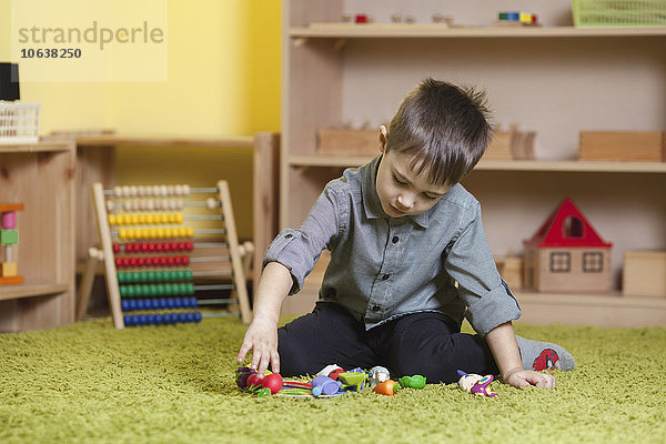 Volle Länge des Jungen  der mit Spielzeug auf dem Teppich im Klassenzimmer spielt.