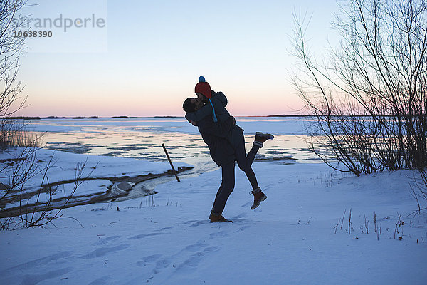 Volle Länge des jungen Mannes  der die Frau aufnimmt und auf dem schneebedeckten Feld küsst.