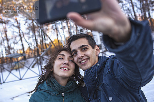 Fröhliches junges Paar  das im Winter Selfie durchs Smartphone nimmt.