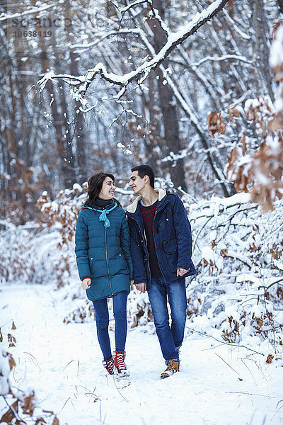 Volle Länge des liebenden jungen Paares in warmer Kleidung auf schneebedecktem Gelände