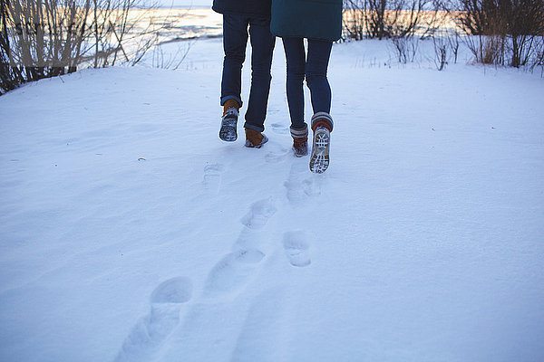 Niedriger Abschnitt eines jungen Paares  das auf einem schneebedeckten Feld läuft.
