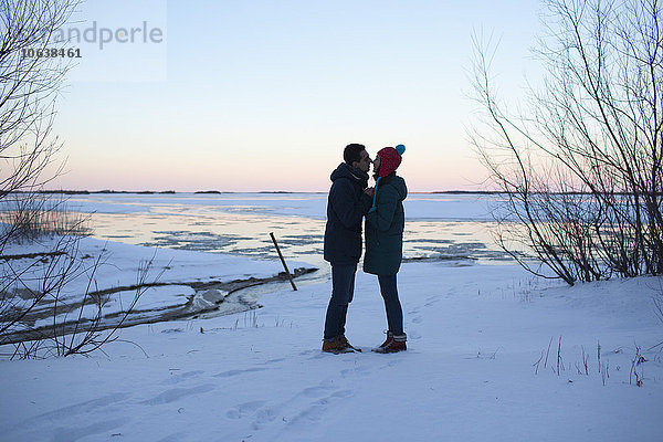 Seitenansicht des jungen Paares  das sich auf dem schneebedeckten Feld küsst.