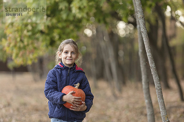 Porträt eines lächelnden Mädchens mit Kürbis im Wald