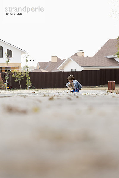 Junge spielt mit Hund auf Fußweg gegen klaren Himmel