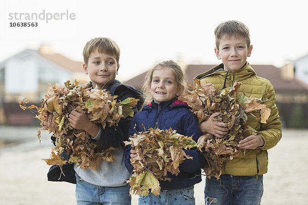 Porträt von glücklichen Jungen und Mädchen mit trockenen Blättern im Freien