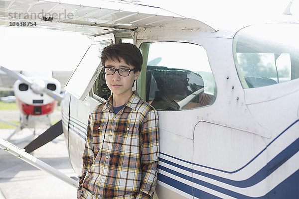Porträt eines selbstbewussten Teenagers  der vor einem Privatflugzeug steht.