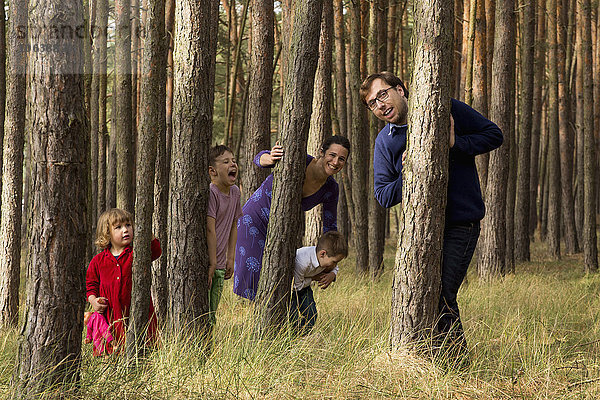 Glückliche Familie versteckt sich hinter Baumstämmen im Wald