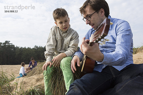 Junge schaut Vater beim Gitarrespielen auf dem Feld an