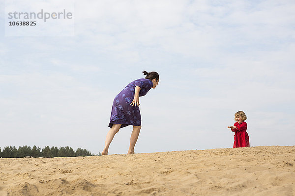 Mutter und Tochter spielen auf Sand gegen den Himmel