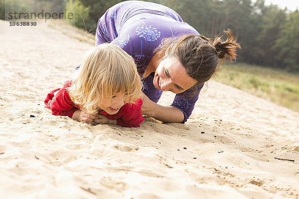 Glückliche Mutter spielt mit Tochter auf Sand