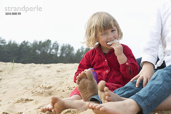 Porträt eines süßen Mädchens beim Sitzen mit der Familie auf Sand