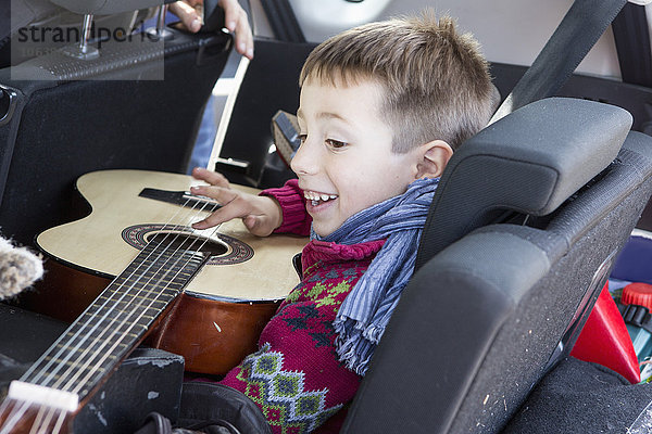 Seitenansicht des glücklichen Jungen beim Gitarrespielen im Auto