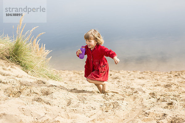 Fröhliches Mädchen mit Wasserflasche beim Laufen auf der Sanddüne