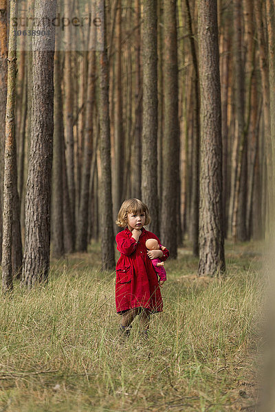 Mädchen schaut weg  während sie die Puppe im Wald hält.