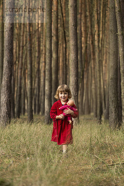 Porträt eines süßen Mädchens  das eine Puppe hält  während es im Wald steht.