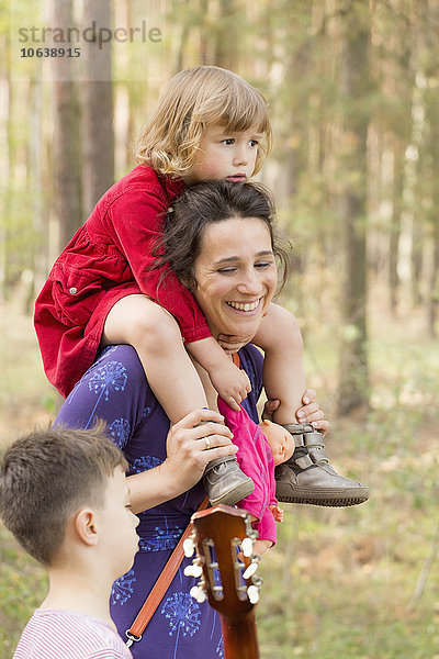 Glückliche Frau  die eine Tochter trägt  während sie mit ihrem Sohn im Wald redet.