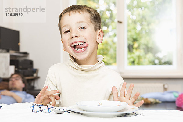 Porträt des süßen Jungen  der die Zunge am Tisch herausstreckt.