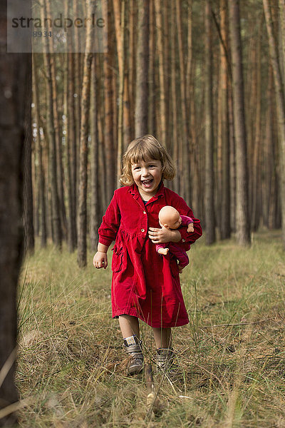 Glückliches Mädchen hält Puppe beim Waldspaziergang