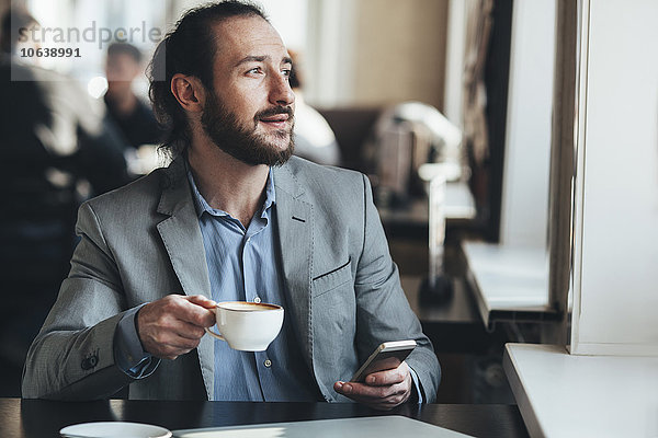 Mittlerer erwachsener Geschäftsmann mit Kaffeetasse und Handy im Café