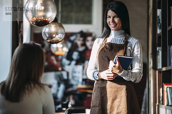 Fröhliche Kellnerin im Gespräch mit Kundin im Coffee-Shop