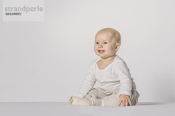 Fröhliches kleines Mädchen sitzend vor weißem Hintergrund