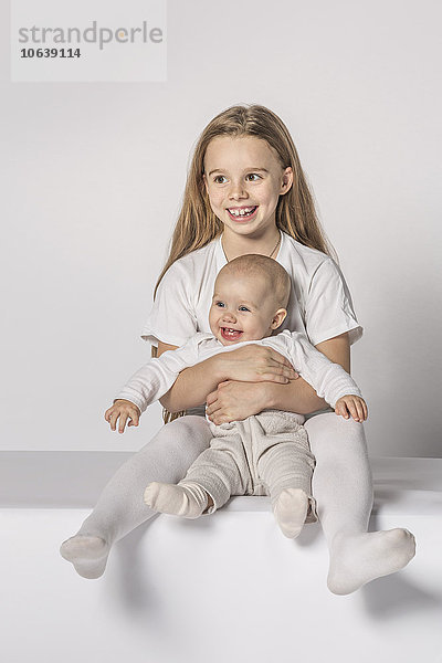 Fröhliches kleines Mädchen sitzend mit Schwester auf weißem Hintergrund