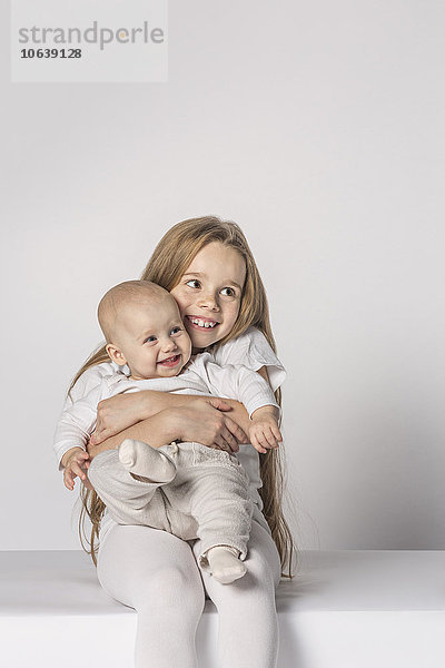 Fröhliches kleines Mädchen sitzend mit Schwester auf weißem Hintergrund