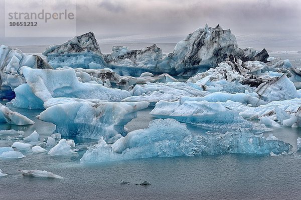 Treibende blaue Eisberge in der Gletscherlagune Jökulsarlon bei Nebel  hinten der Gletscher Vatnajökull  Südisland  Island  Europa
