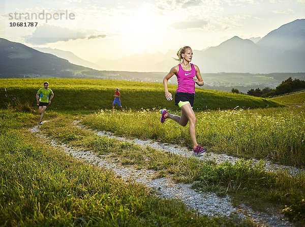 Junge Frau  20-25 Jahre  läuft auf einem Weg durch Wiesen  hinten weitere Läufer  Rosengarten  Patsch  Tirol  Österreich  Europa