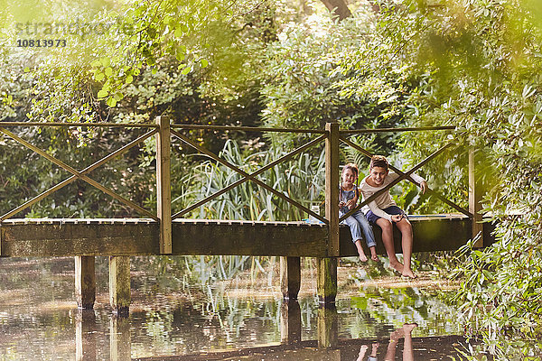 Bruder und Schwester sitzen auf einer Fußgängerbrücke im Park mit Bäumen.