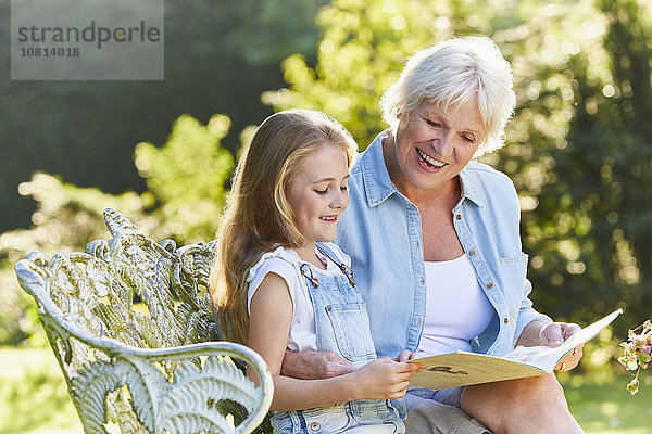 Großmutter beim Lesen mit Enkelin auf der Gartenbank