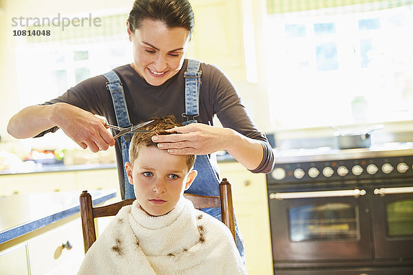 Unglücklicher Junge bekommt Haarschnitt von Mutter in der Küche