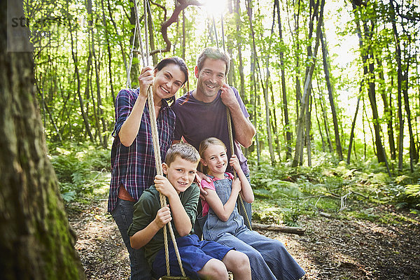 Portrait lächelnde Familie bei Seilschaukel im Wald
