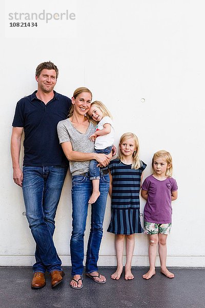 Porträt von Eltern und drei jungen Töchtern  die vor der weißen Wand stehen