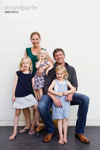 Familienporträt von Eltern und drei jungen Töchtern vor der weißen Wand