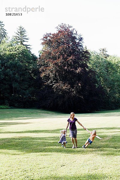 Mittlere erwachsene Frau und zwei Töchter  die Händchen halten und im Park rennen.