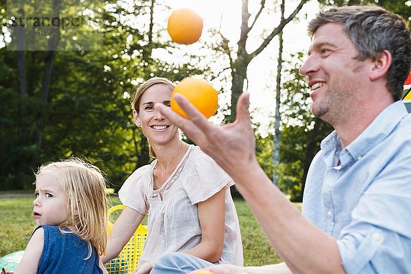 Reifer Mann jongliert mit Orangen beim Familienpicknick im Park