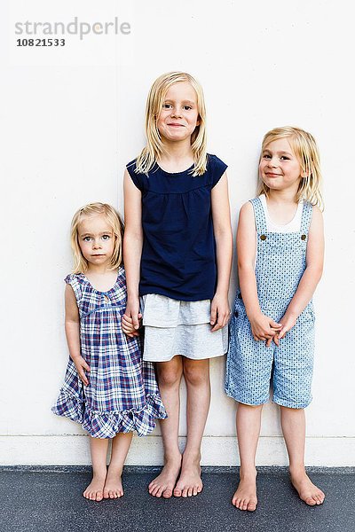Porträt von drei jungen Schwestern  die vor der weißen Wand stehen