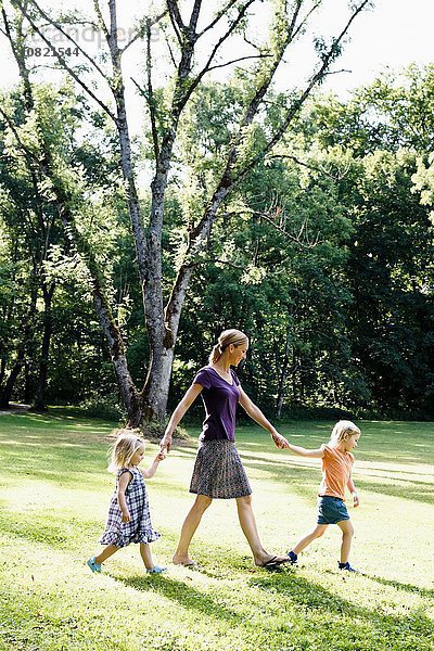 Mittlere erwachsene Frau  die mit zwei Töchtern im Park Händchen hält.
