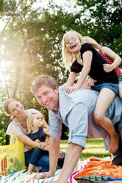 Vater schenkt Töchtern Huckepack beim Familienpicknick im Park