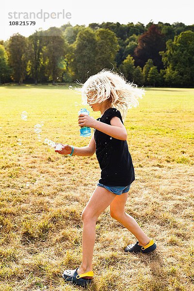 Mädchen winkt Blasenstab und macht Blasen im Park