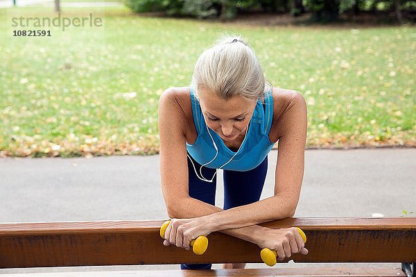 Reife Frau macht eine Pause auf der Parkbank während des Trainings im Park