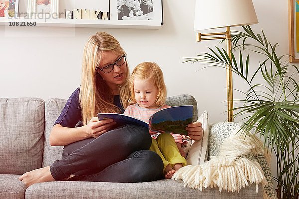 Mittlere erwachsene Frau und Kleinkind Tochter beim Lesen auf dem Sofa