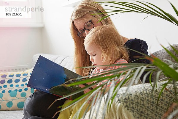 Mittlere erwachsene Frau und Kleinkind Tochter lesen auf dem Wohnzimmersofa