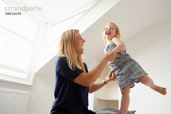 Mittlere erwachsene Frau und Kleinkind-Tochter tanzen auf dem Bett